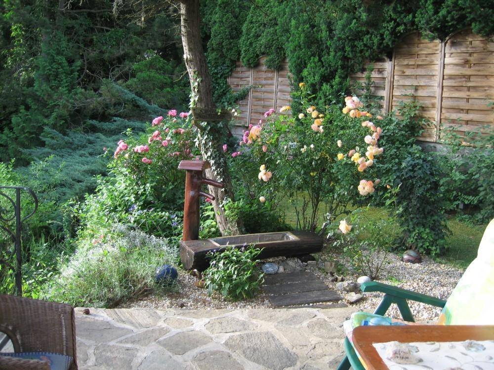 Gemütliche Terrasse mit Natursteinboden, Gartenmöbeln und blühenden Rosenbüschen im Sonnenlicht.