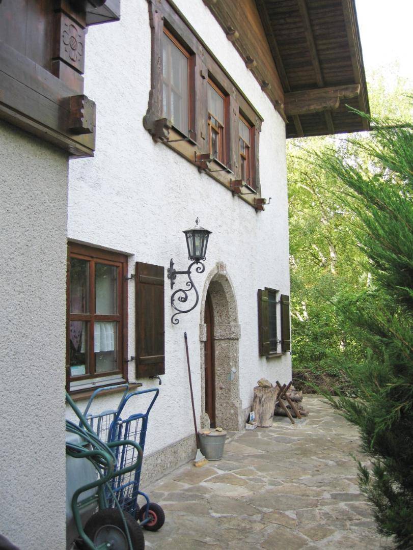 Seitenansicht des Hauses mit gewölbtem Eingang, Natursteinweg und traditionellen Fensterläden.