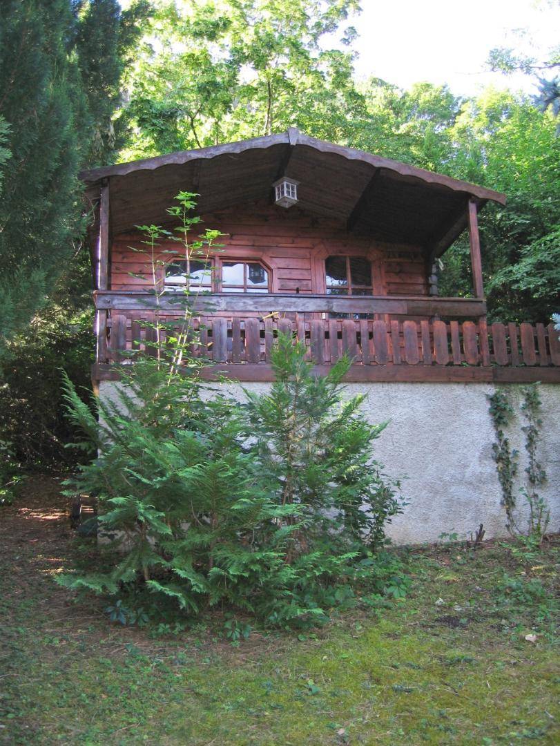 Rustikales Gartenhaus aus Holz mit kleiner Veranda, eingebettet im Grünen des Gartens.