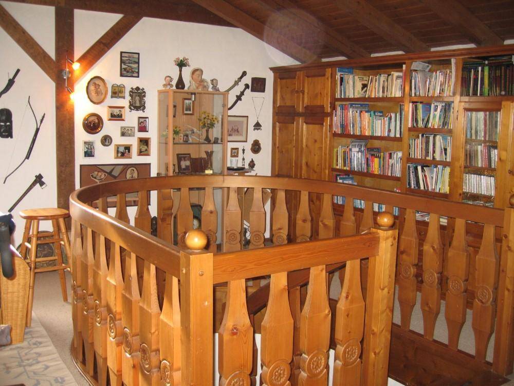 Galeriebereich mit Holzgeländer und integrierten Bücherregalen, unter sichtbaren Dachschrägen.