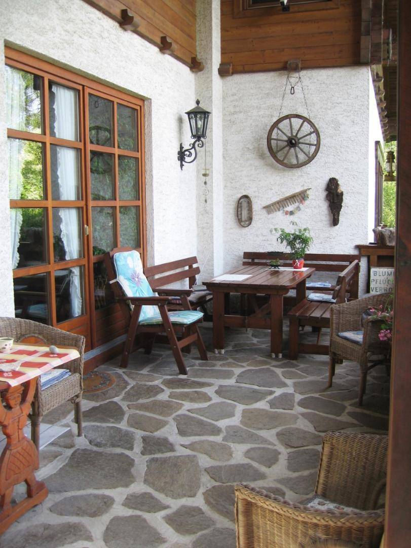 Überdachte Loggia mit Natursteinboden und rustikalen Holzmöbeln für entspannte Stunden im Freien.