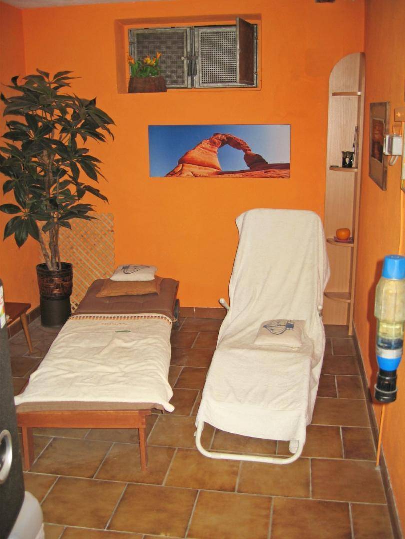 Raum mit orangefarbenen Wänden, zwei Liegen und Fliesenboden, ideal als Wellnessbereich.