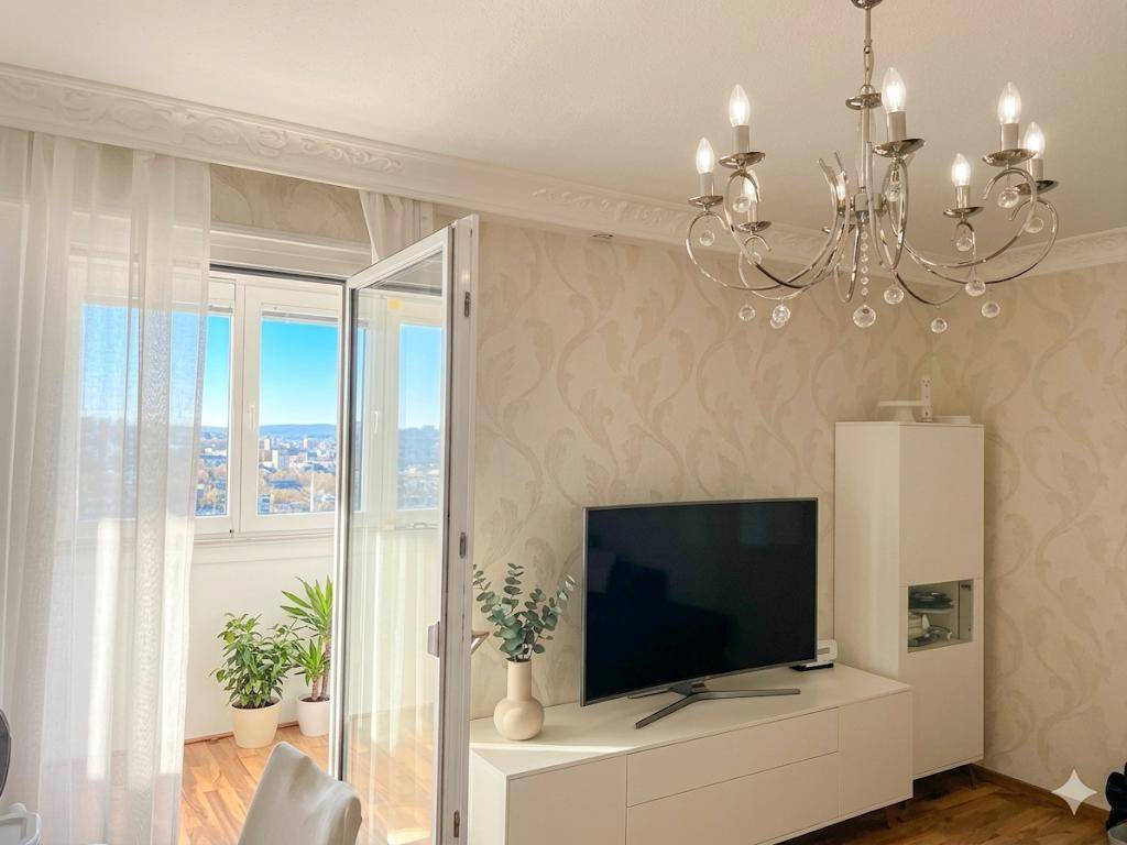 Gemütlicher Wohnbereich mit Fernseher, Pflanzen und Zugang zu einem Balkon mit Weitblick.