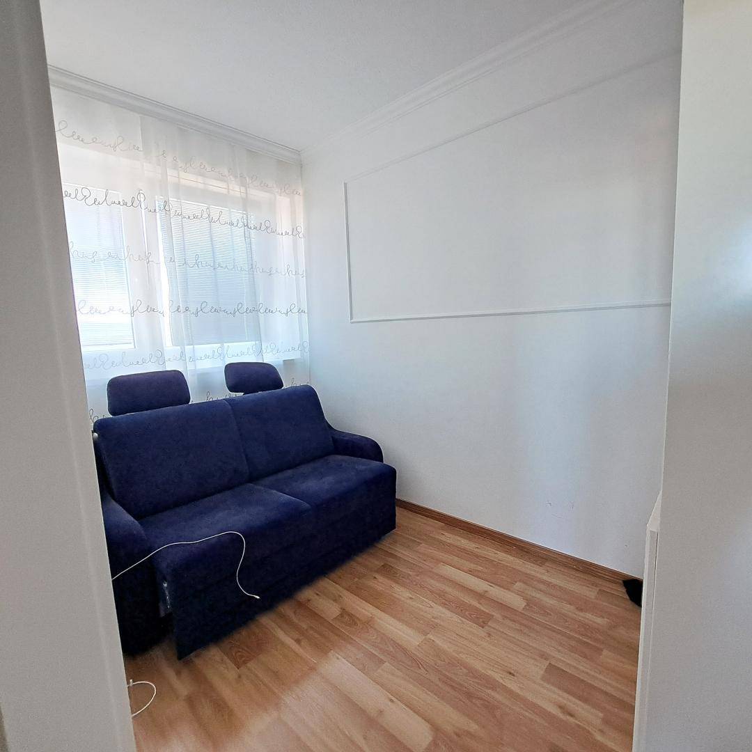 Kleiner, heller Raum mit blauem Sofa und Holzfußboden, ideal als Gäste- oder Arbeitszimmer.