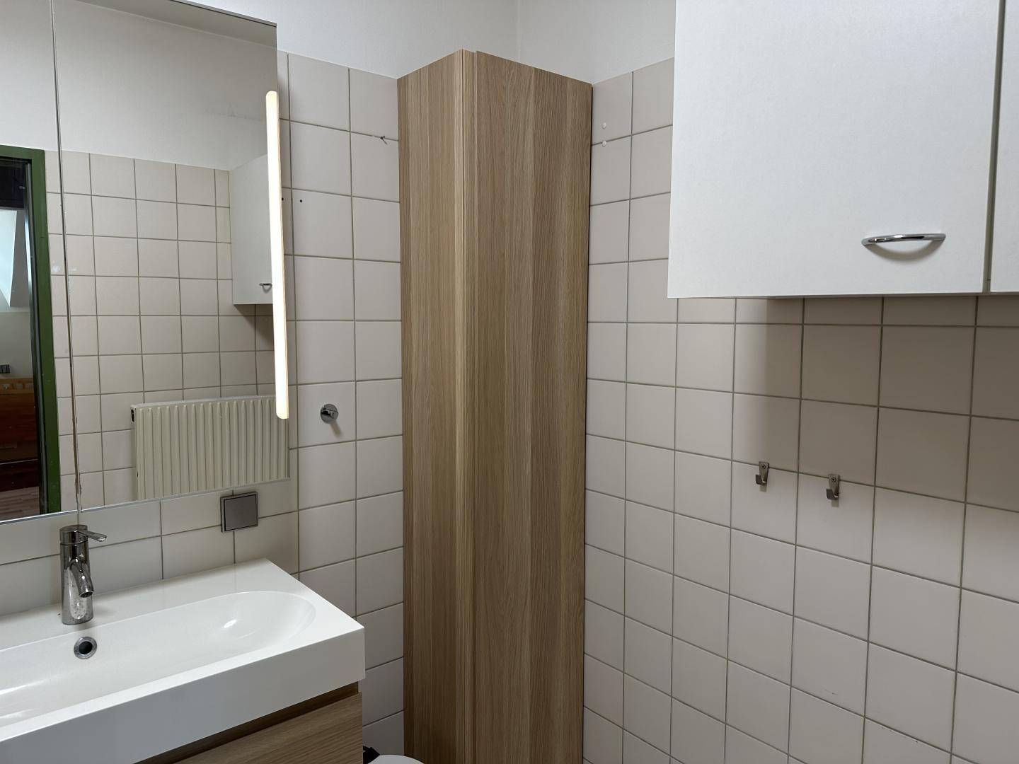 Modernes Badezimmer mit Waschbecken, beleuchtetem Spiegelschrank und hohen Holzschränken.