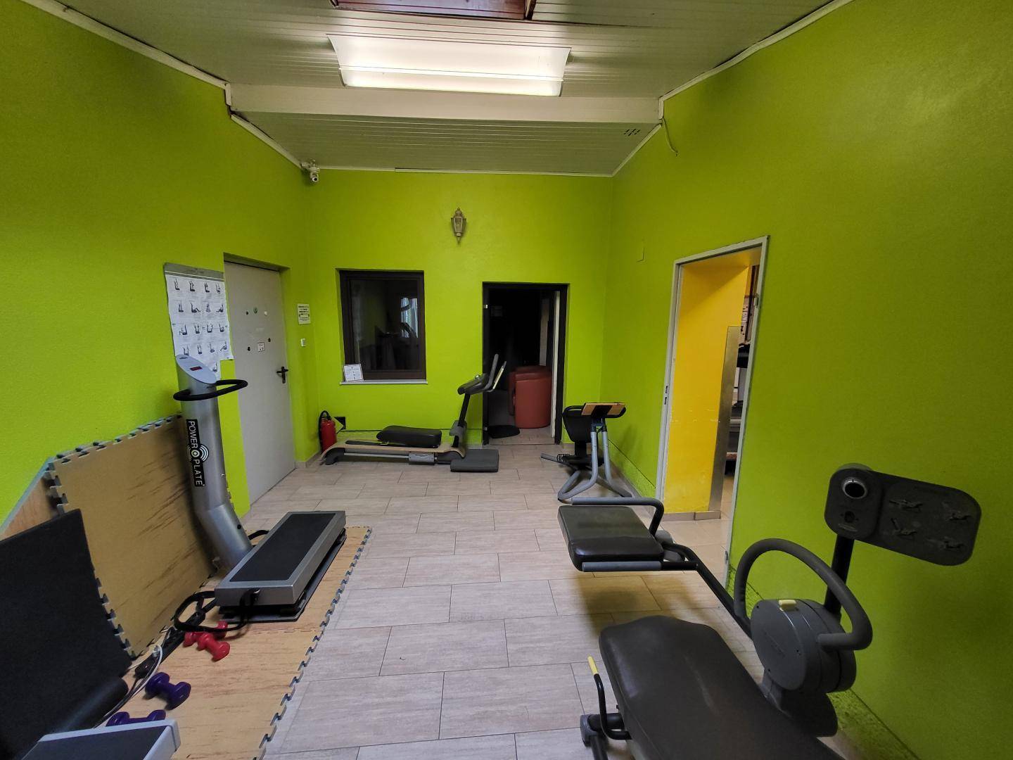 Kleinerer Fitnessbereich mit grünen Wänden, Trainingsgeräten und Fliesenboden.