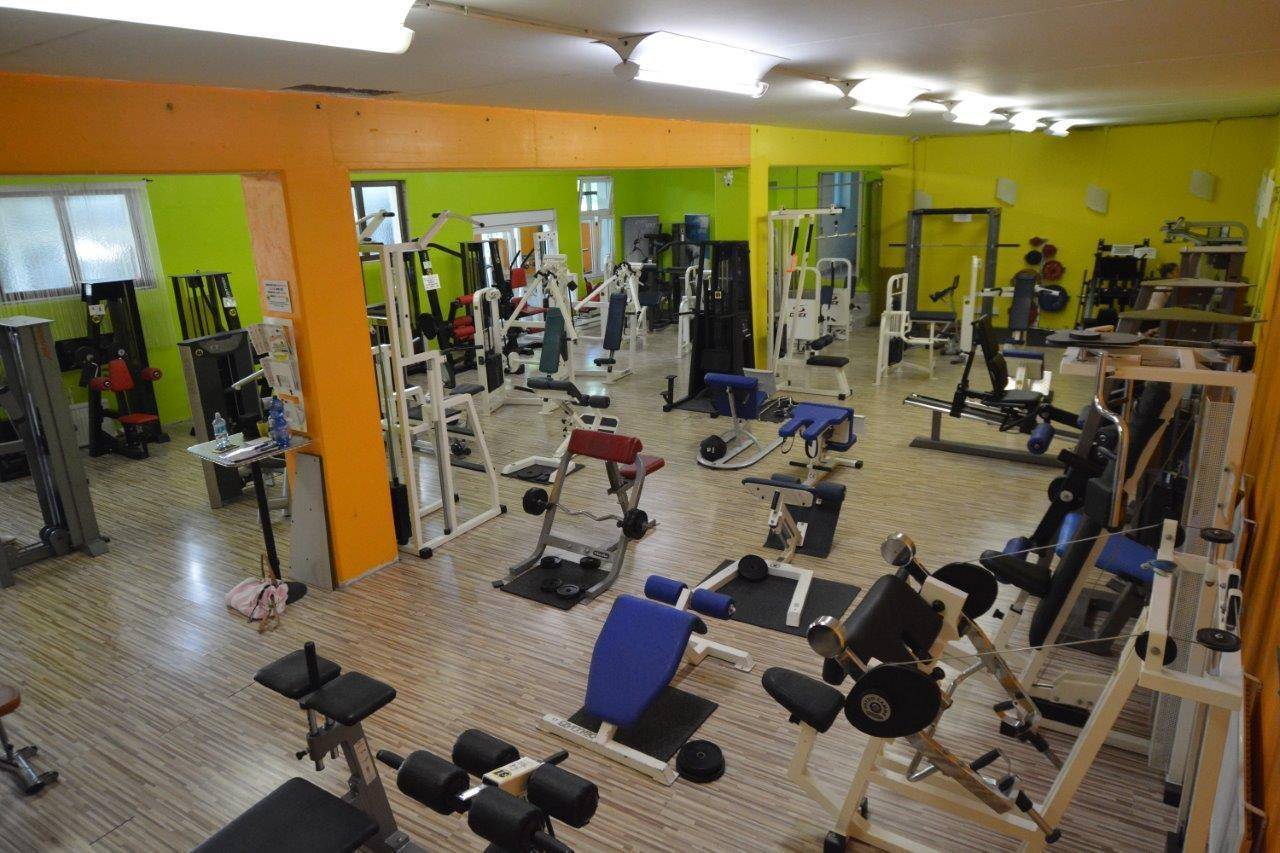 Großer Fitnessraum mit einer Vielzahl von Krafttrainingsgeräten und hellen Wänden.