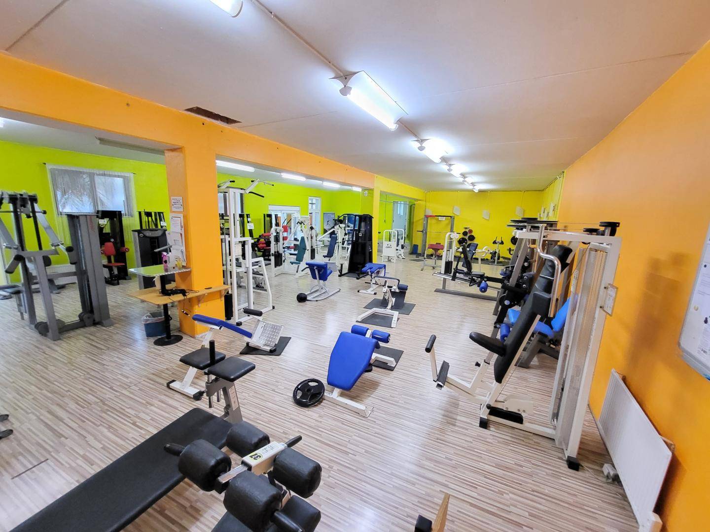 Geräumiger Fitnessraum mit verschiedenen Trainingsgeräten und gelb-grünen Wänden.