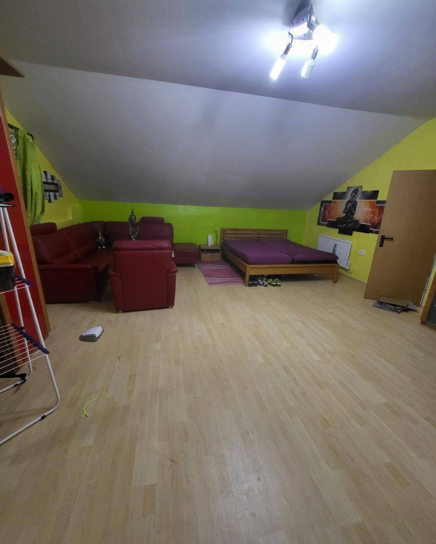 Schlafzimmer im Dachgeschoss mit schrägen Wänden, Doppelbett und rotem Sofa.