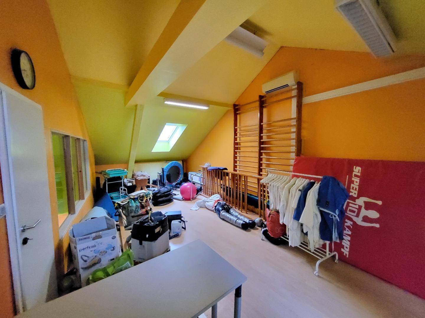Dachbodenraum mit schrägen Wänden, Sprossenwand und verschiedenen Gegenständen, hell beleuchtet.