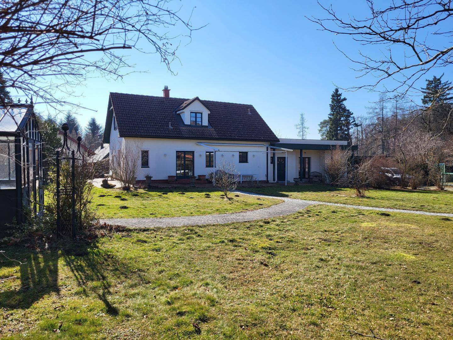 Ansicht des Hauses von der Gartenseite mit weitläufigem Rasen, gepflasterten Wegen und einem Gewächshaus.