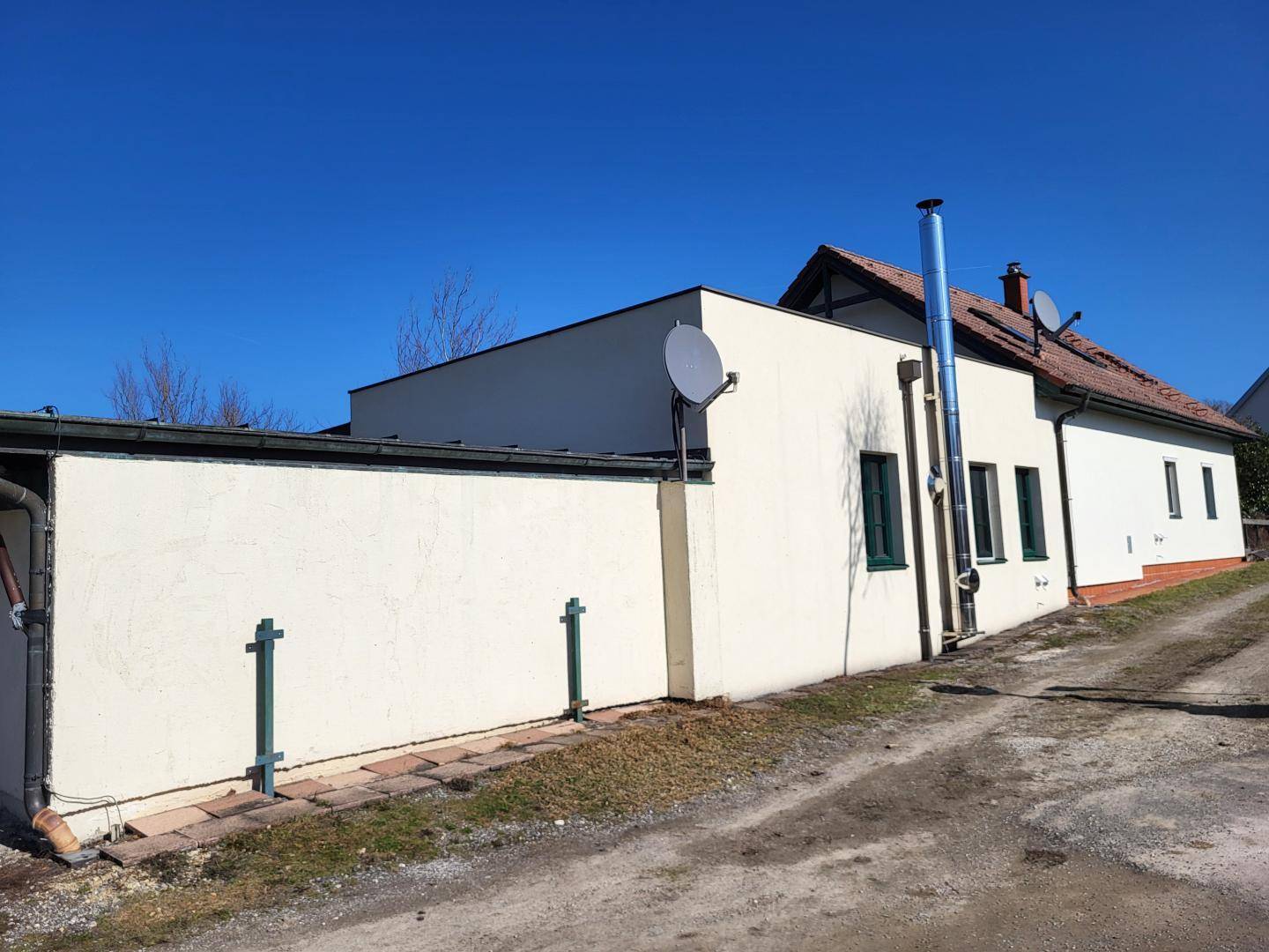 Seitenansicht des Hauses mit einem Anbau, Flachdach und einem modernen Edelstahlkamin.