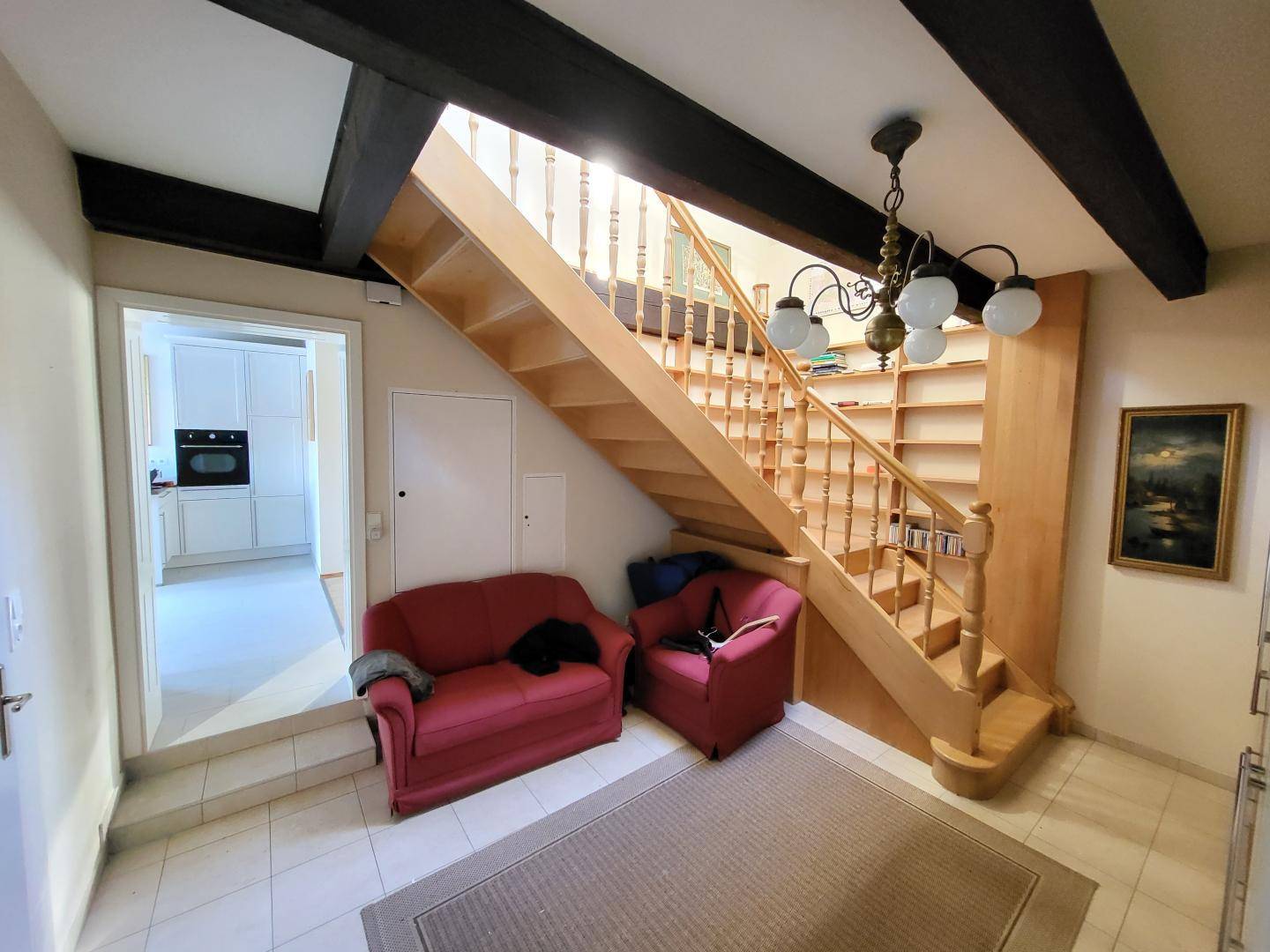 Eingangsbereich mit Holztreppe, kleinen Sofas und Fliesenboden, mit Blick in die angrenzende Küche.