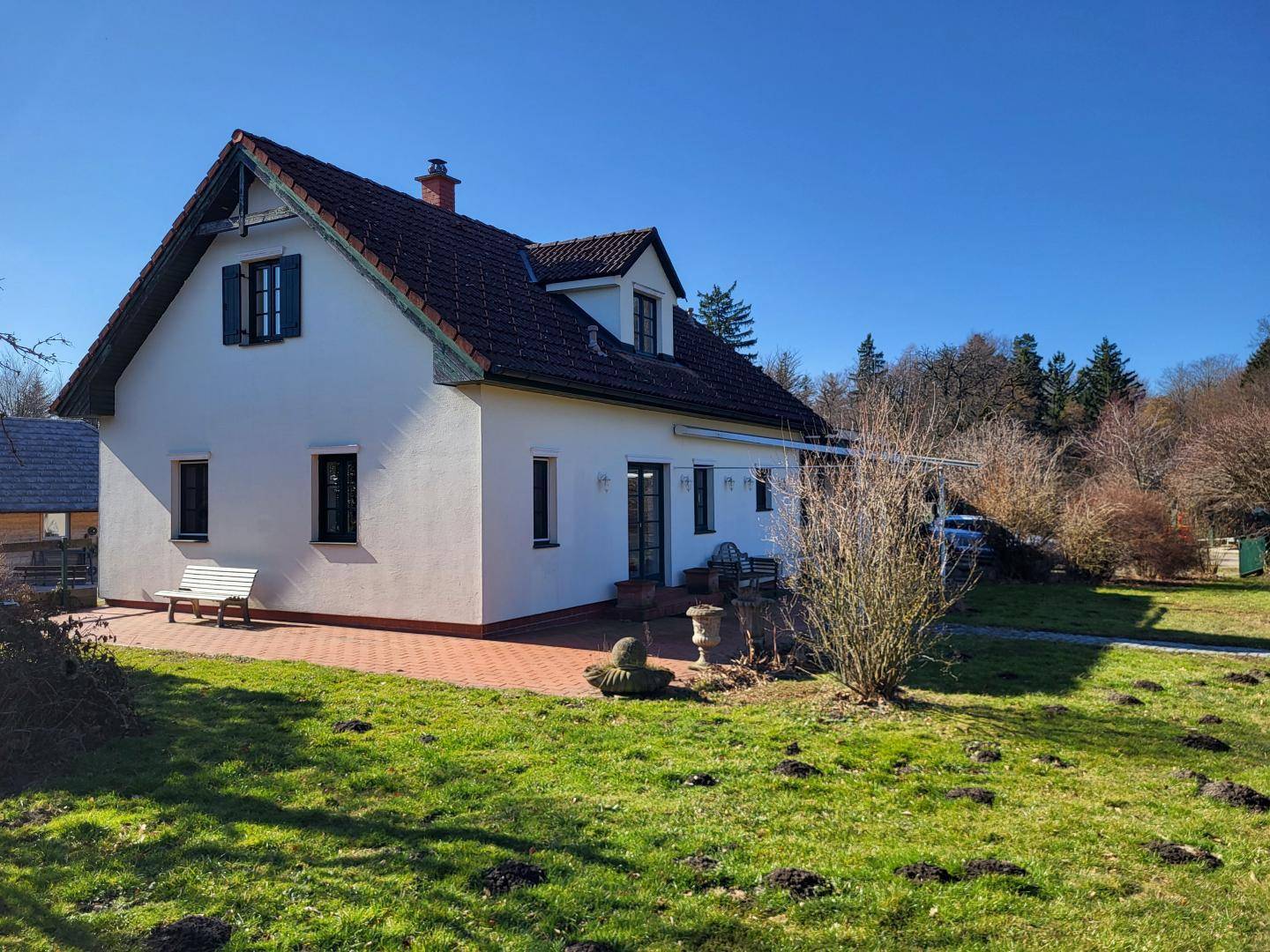 Seitenansicht des Hauses mit einer großen gepflasterten Terrasse und einem weitläufigen Rasenbereich.
