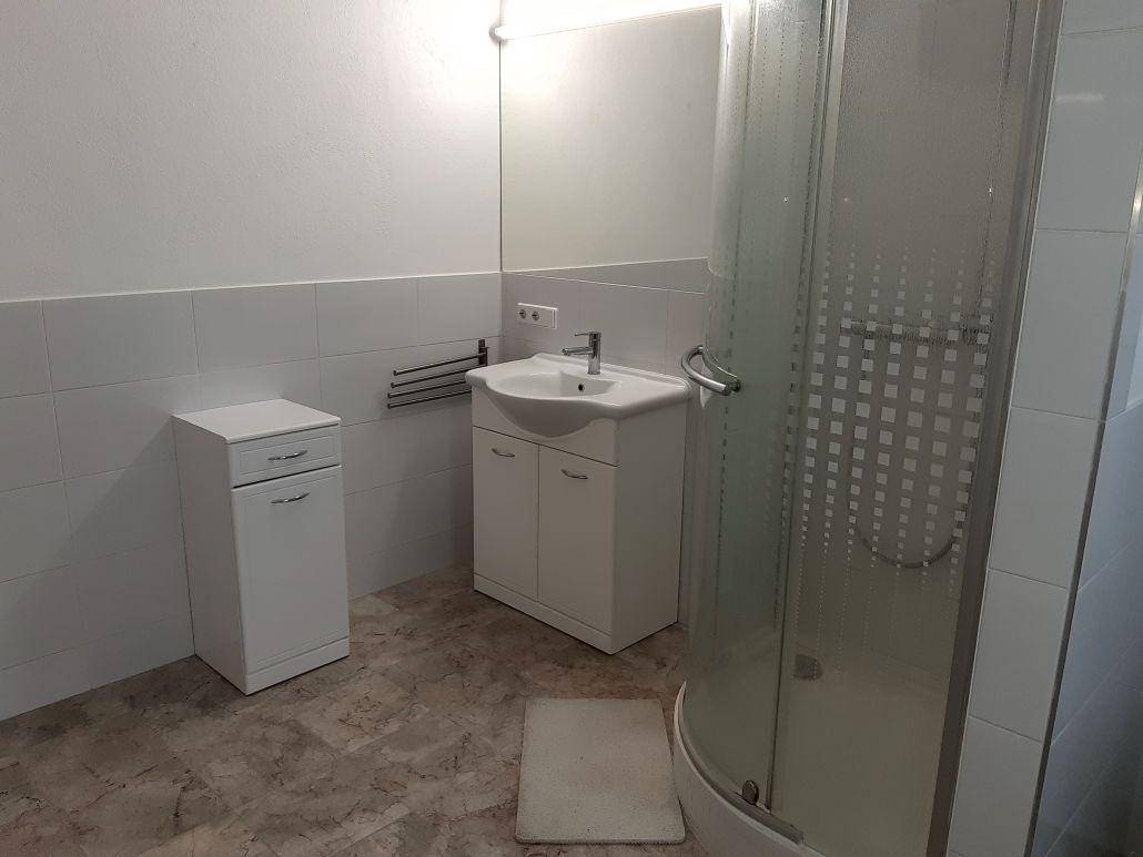 Helles Badezimmer mit modernem Waschbecken, Spiegel und Duschkabine, in gutem Zustand.