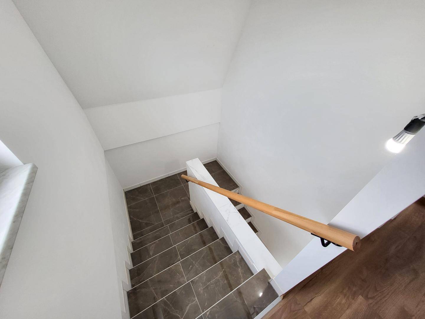Treppenhaus mit gefliesten Stufen und Holzhandlauf, das die verschiedenen Etagen verbindet.