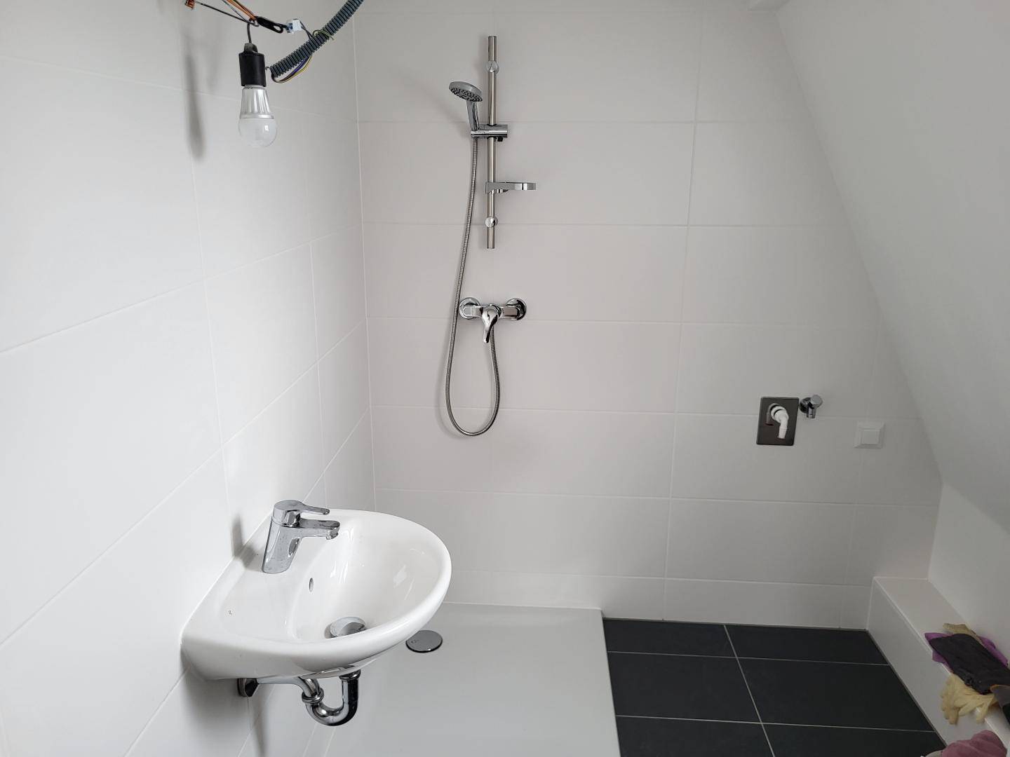 Modernes Badezimmer mit Dusche, Waschbecken und weißen Fliesen unter einer Dachschräge.