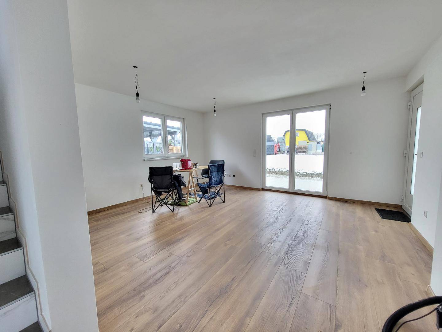Heller, offener Wohnbereich mit Laminatboden und großen Glastüren zum Außenbereich.