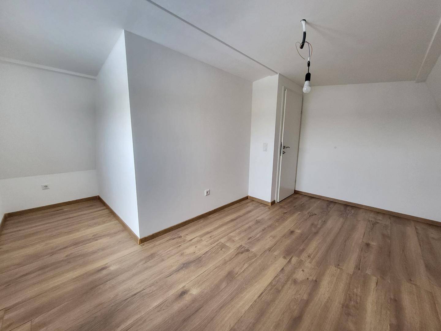 Helles Zimmer im Obergeschoss mit Laminatboden, Dachschräge und weiß gestrichenen Wänden.