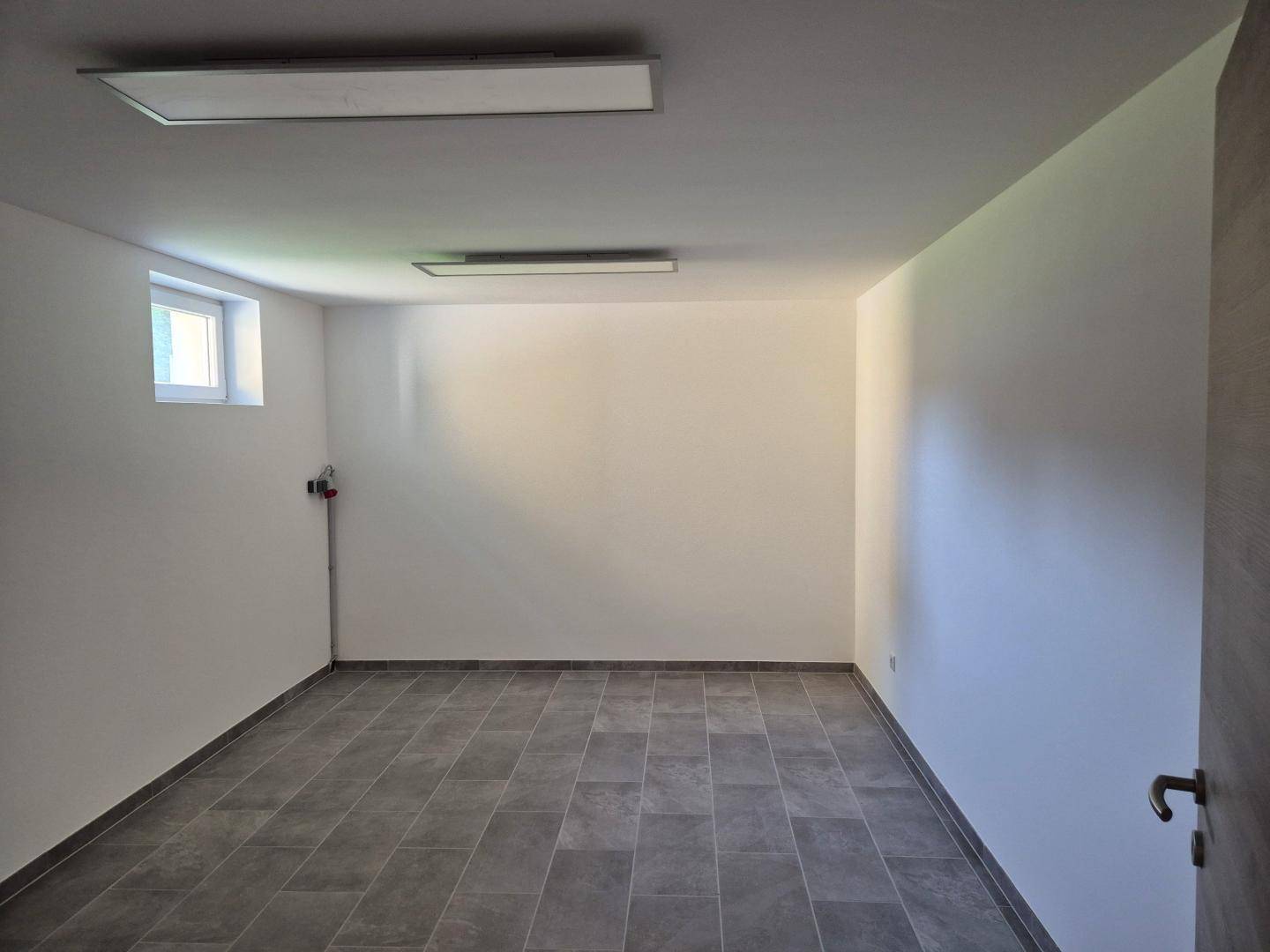 Geräumiger Kellerraum mit Fliesenboden und kleinem Fenster, ideal als Lagerfläche.
