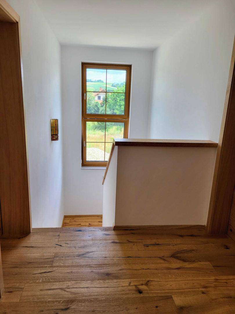 Heller Treppenabsatz mit Holzboden und Fenster, das einen weiten Blick ins Grüne bietet.