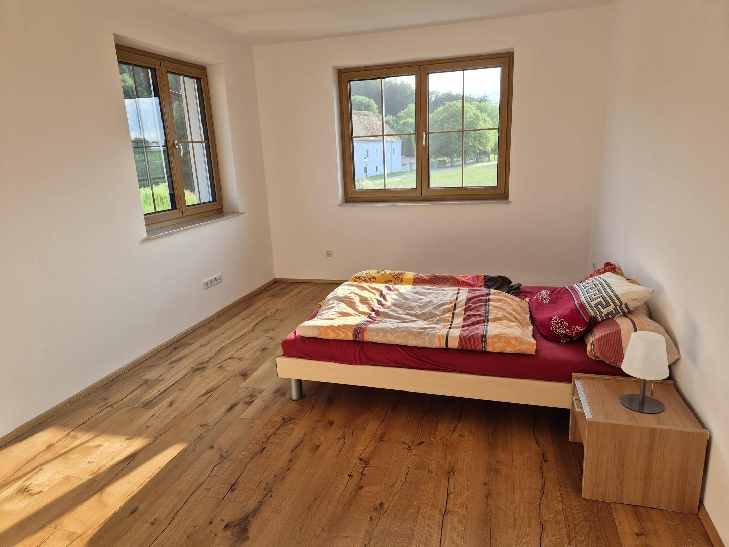 Schlafzimmer mit Holzboden, Doppelbett und Fenstern mit Blick auf die Landschaft.