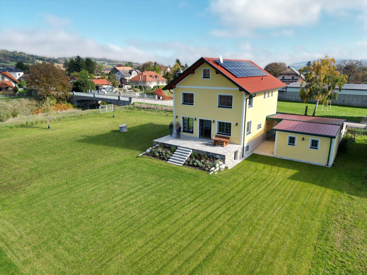 Luftaufnahme des gelben Hauses mit rotem Dach, Photovoltaikanlage und weitläufigem Garten.