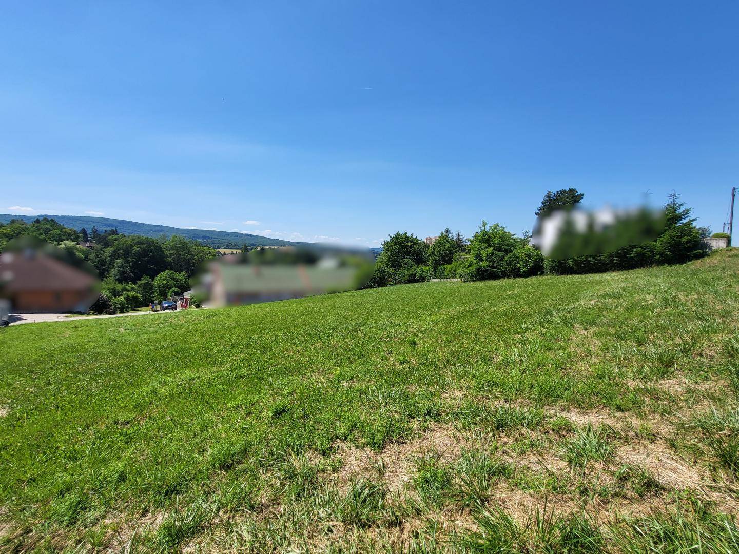 Hügeliges grünes Grundstück unter blauem Himmel mit weitem Blick in die Natur.