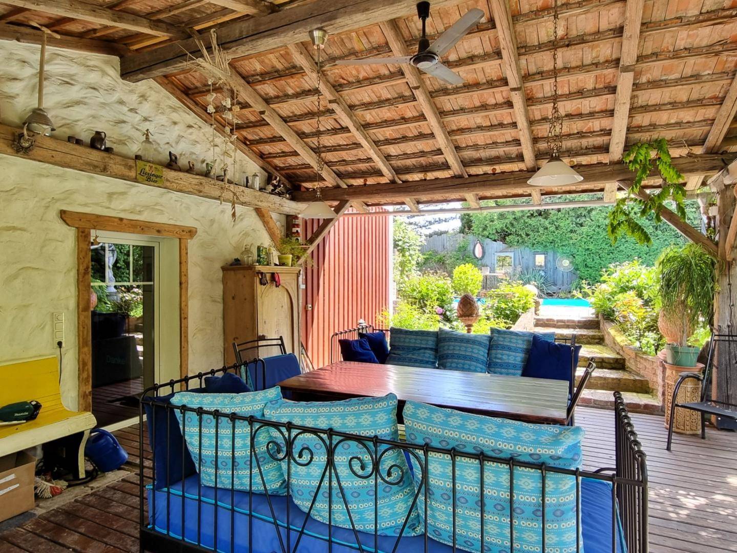 Überdachte Terrasse mit gemütlicher Sitzecke, Holzbalken und Blick in den grünen Garten.