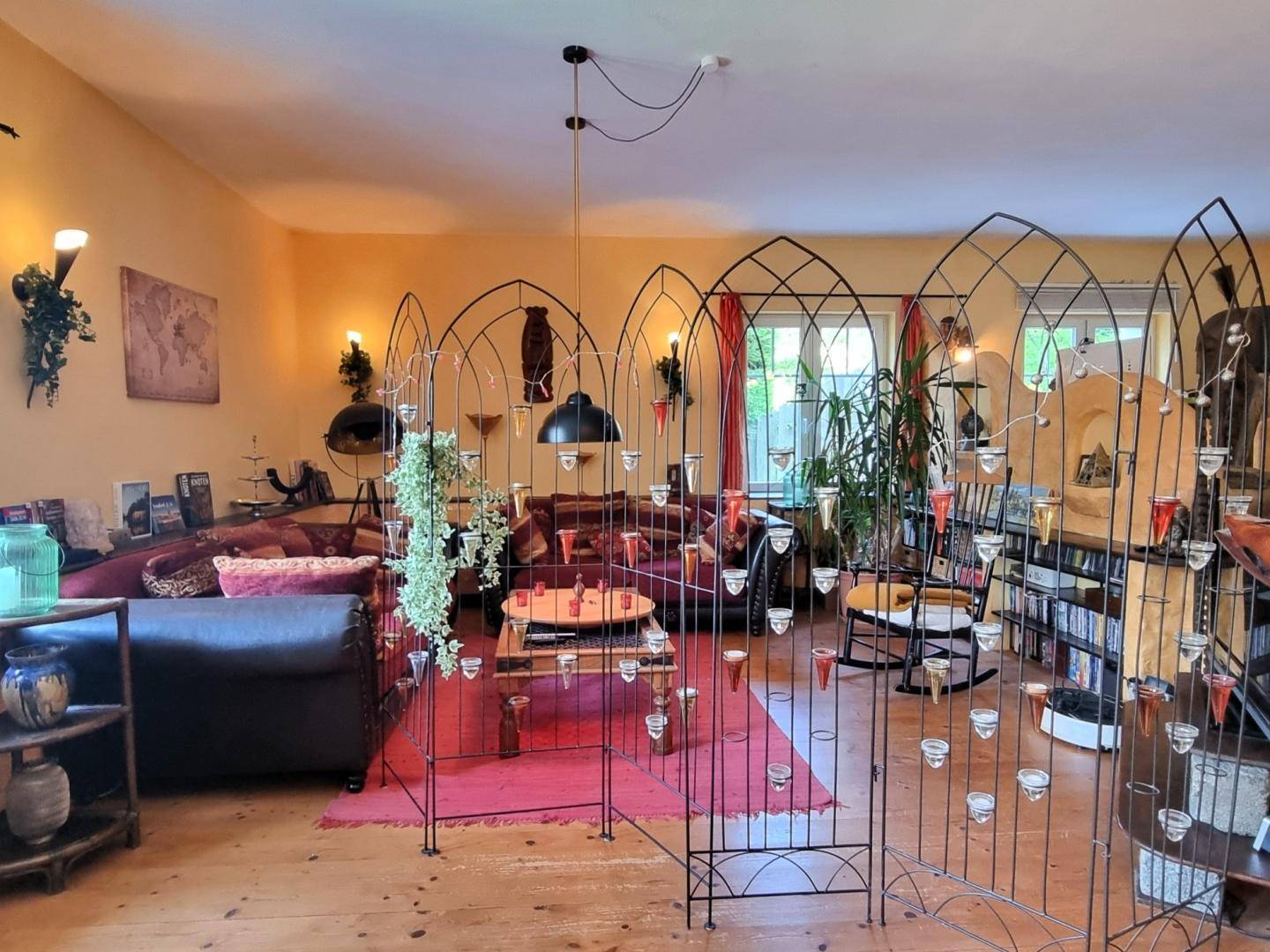 Gemütlicher Wohnbereich mit roten Sofas, Holzboden und dekorativen Metallgittern als Raumteiler.