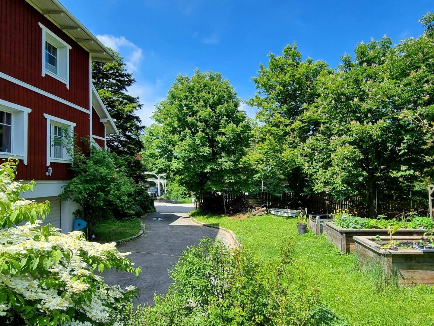 Rotes Holzhaus mit weißer Fassade, umgeben von Bäumen und einem gepflegten Garten.
