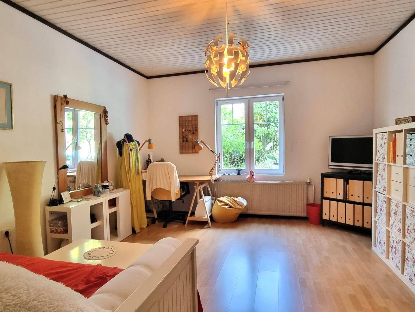 Helles Schlafzimmer mit Holzboden, Schreibtisch und großem Fenster mit Blick ins Grüne.
