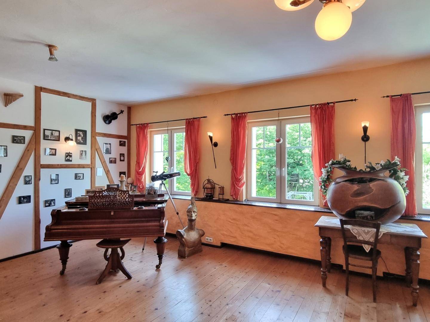 Heller Wohnbereich mit Flügel, Holzboden und großen Fenstern, geschmackvoll mit Kunst dekoriert.