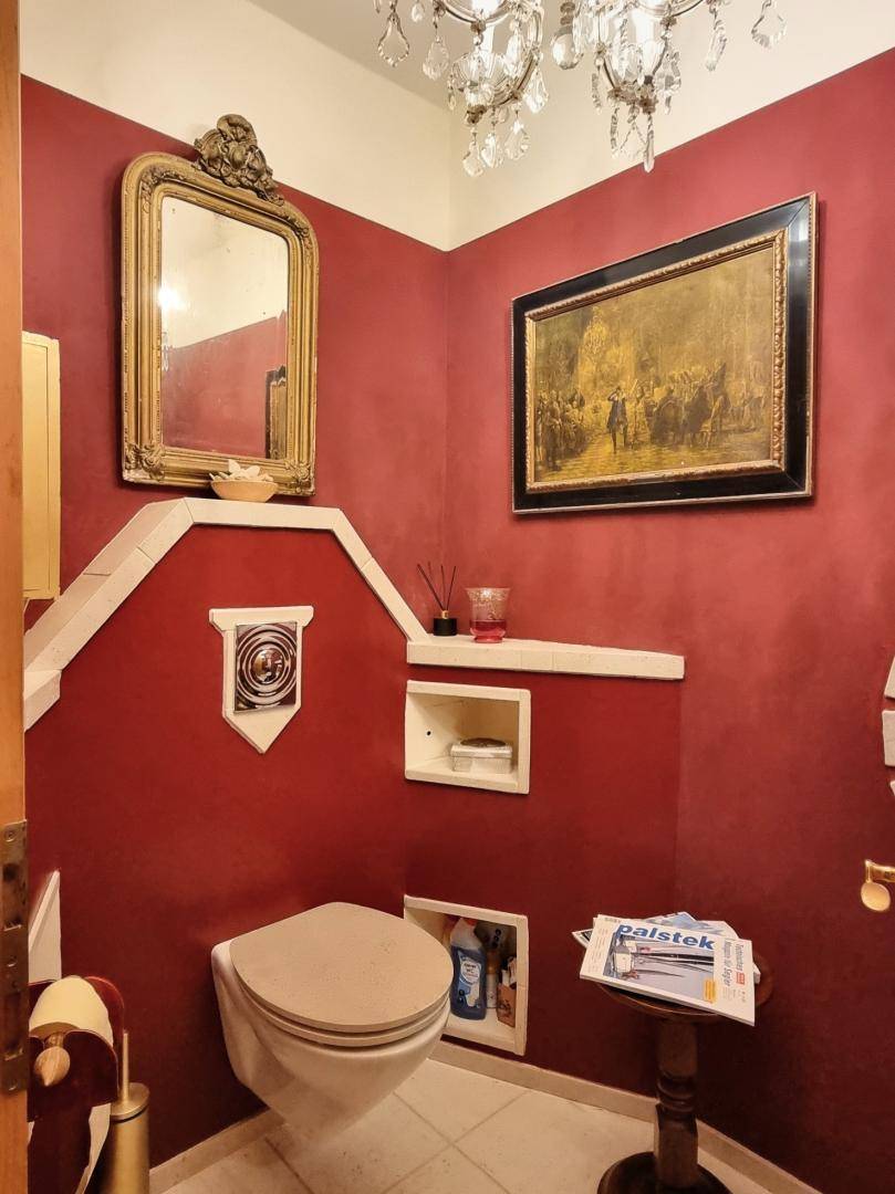 Kleines Gäste-WC mit roter Wandfarbe, Wand-WC und dekorativem Spiegel, elegant gestaltet.