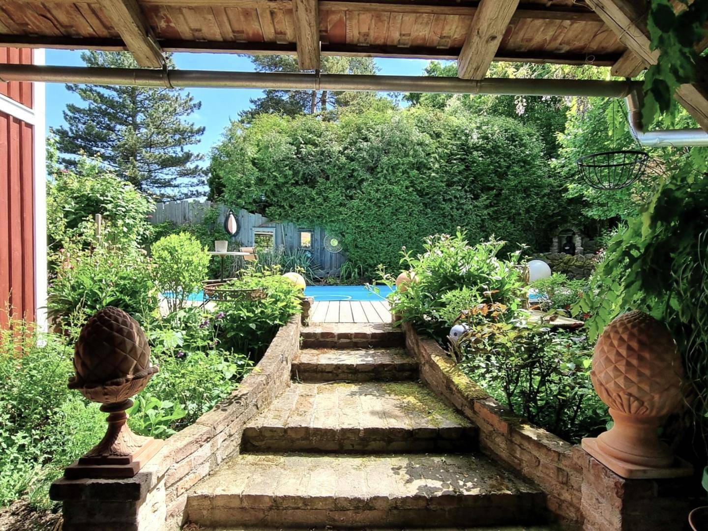 Steinerne Treppe führt durch üppiges Grün zum Poolbereich im sonnigen Garten.