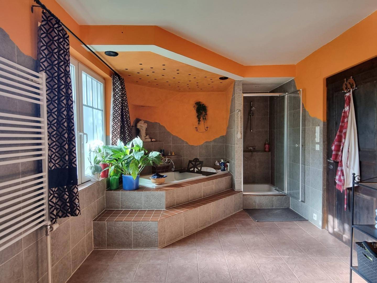 Geräumiges Badezimmer mit Badewanne auf Podest, Dusche und Fenster, farbenfroh und individuell gestaltet.