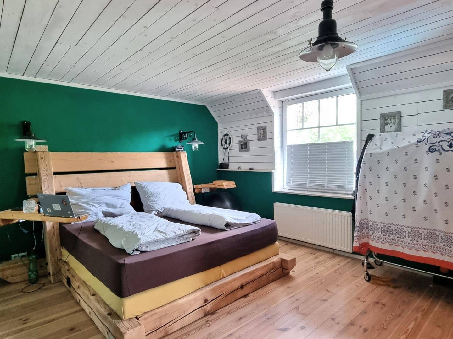 Schlafzimmer mit Holzboden, Holzbett und grüner Akzentwand, hell und gemütlich eingerichtet.