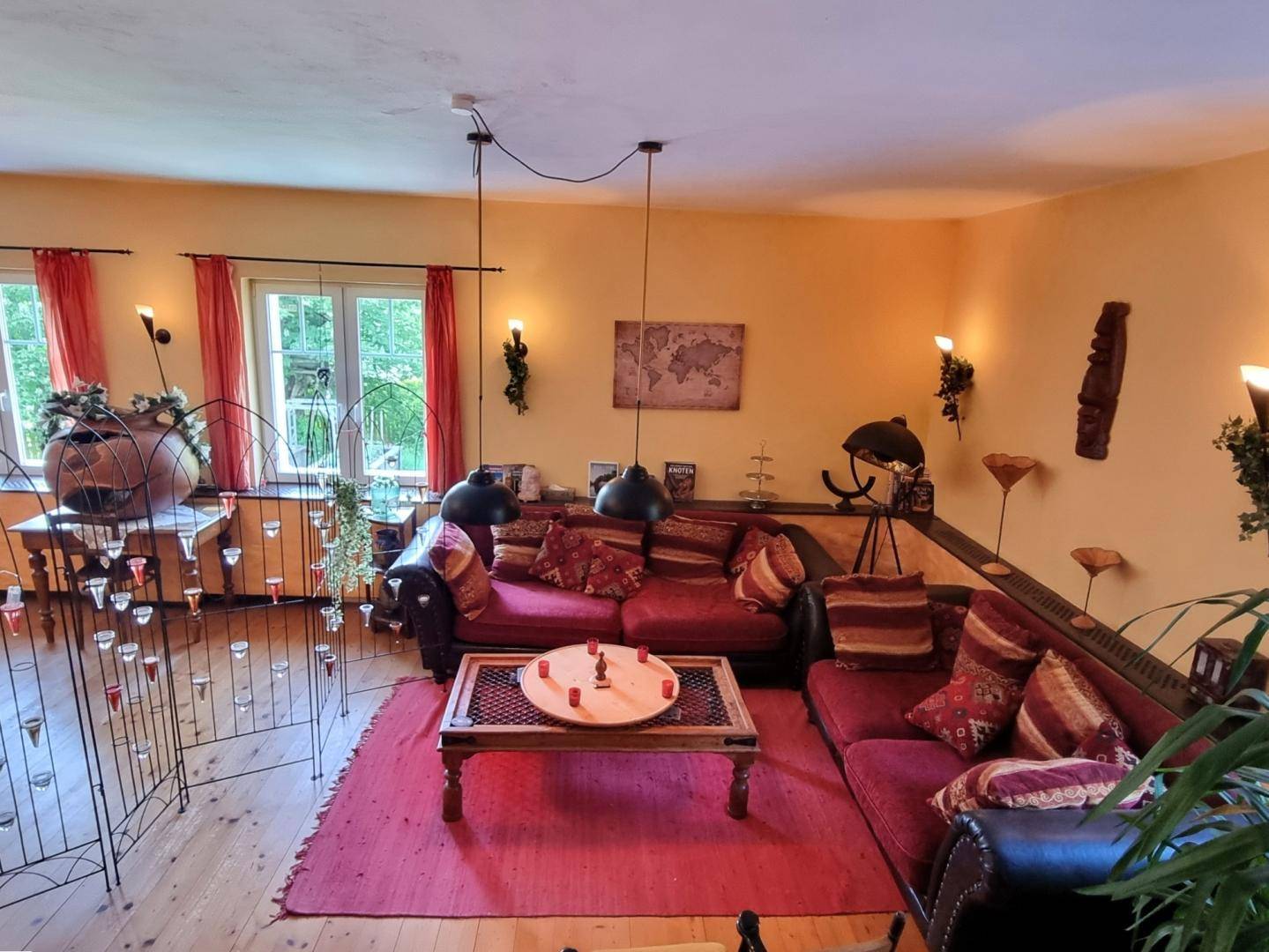Komfortabler Wohnbereich mit roten Sofas, Holztisch und dekorativen Wandleuchten, warm beleuchtet.