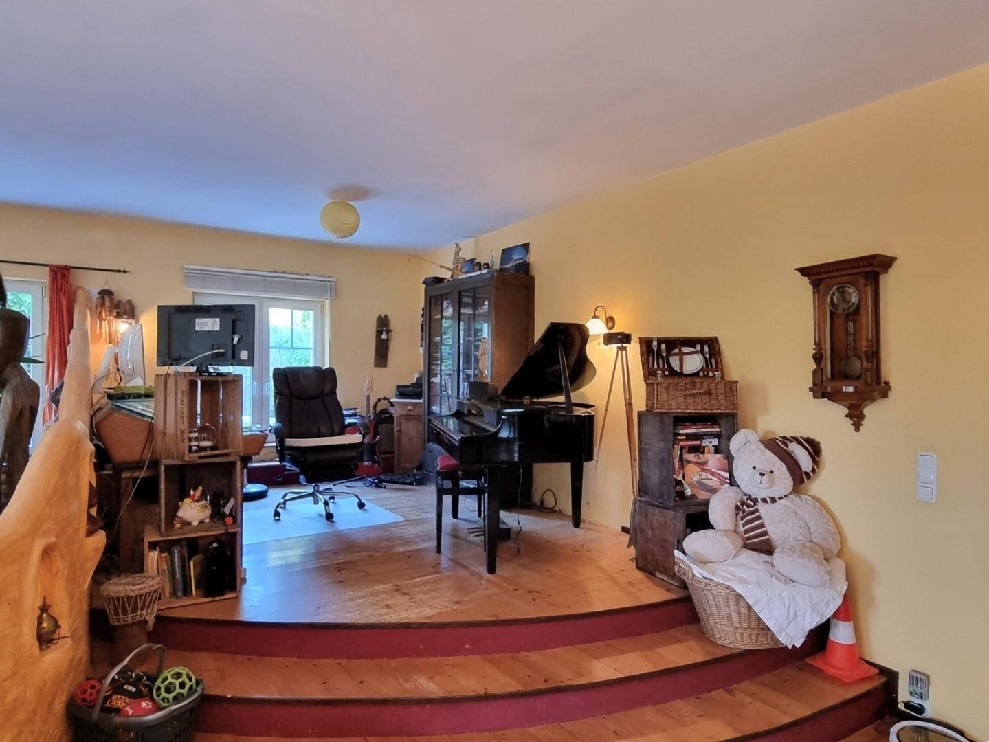 Erhöhter Bereich im Wohnzimmer mit Klavier, Schreibtisch und dekorativen Elementen, hell und geräumig.