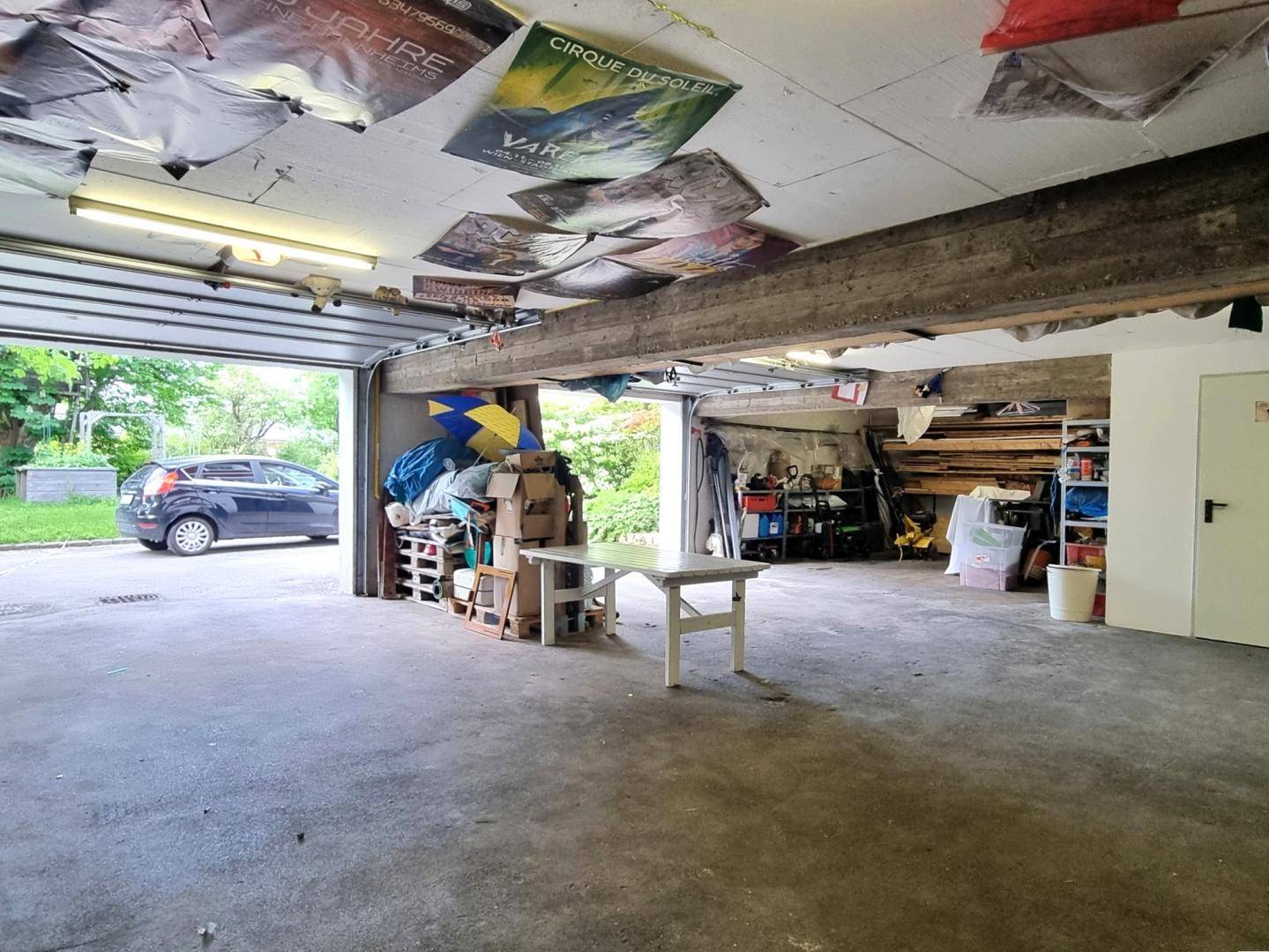Geräumige Garage mit offenem Tor, Betonboden und vielseitigem Stauraum für Fahrzeuge und Material.