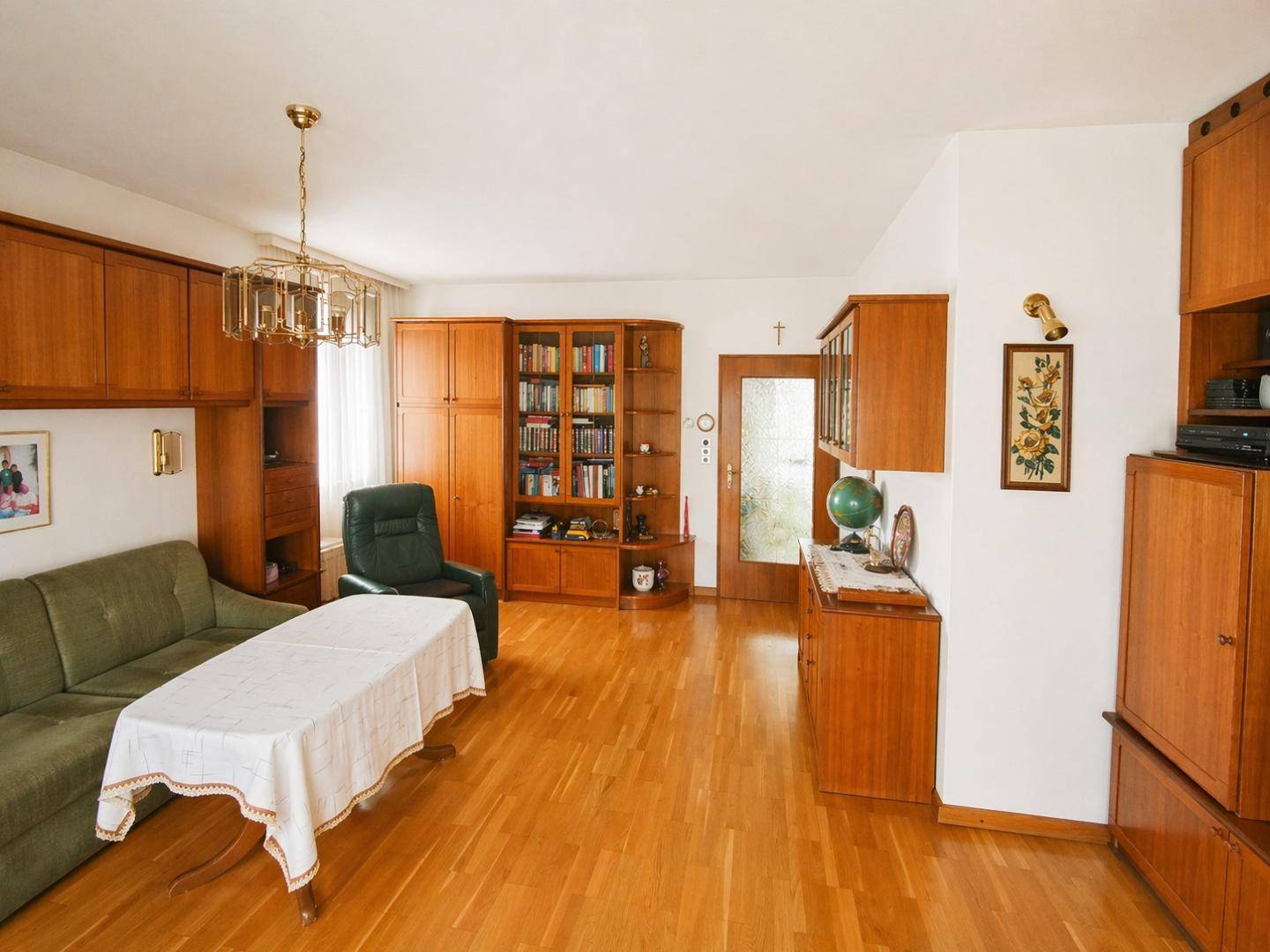 Gemütliches Wohnzimmer mit Holzmöbeln, grünem Sofa und hellem Parkettboden.