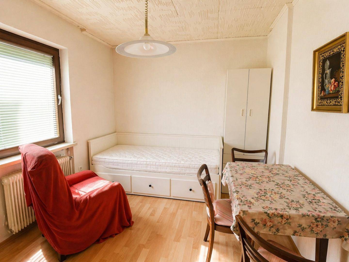 Helles Schlafzimmer oder Gästezimmer mit Einzelbett, rotem Sessel und kleinem Tisch.