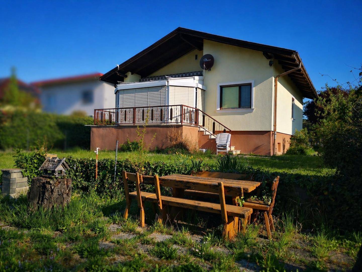 Rückseite des Hauses mit kleiner Terrasse und einem Holztisch im Gartenbereich.