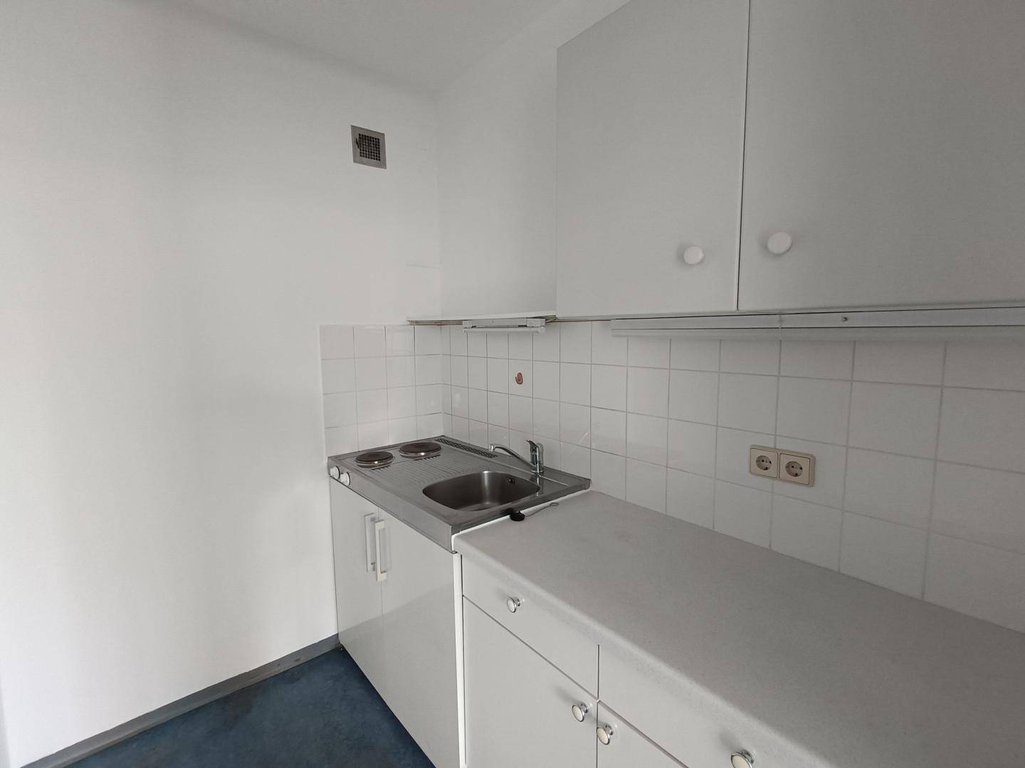 Kleine, funktionale Küchenzeile mit weißen Schränken, Spüle und zwei Kochplatten, sauber und praktisch.