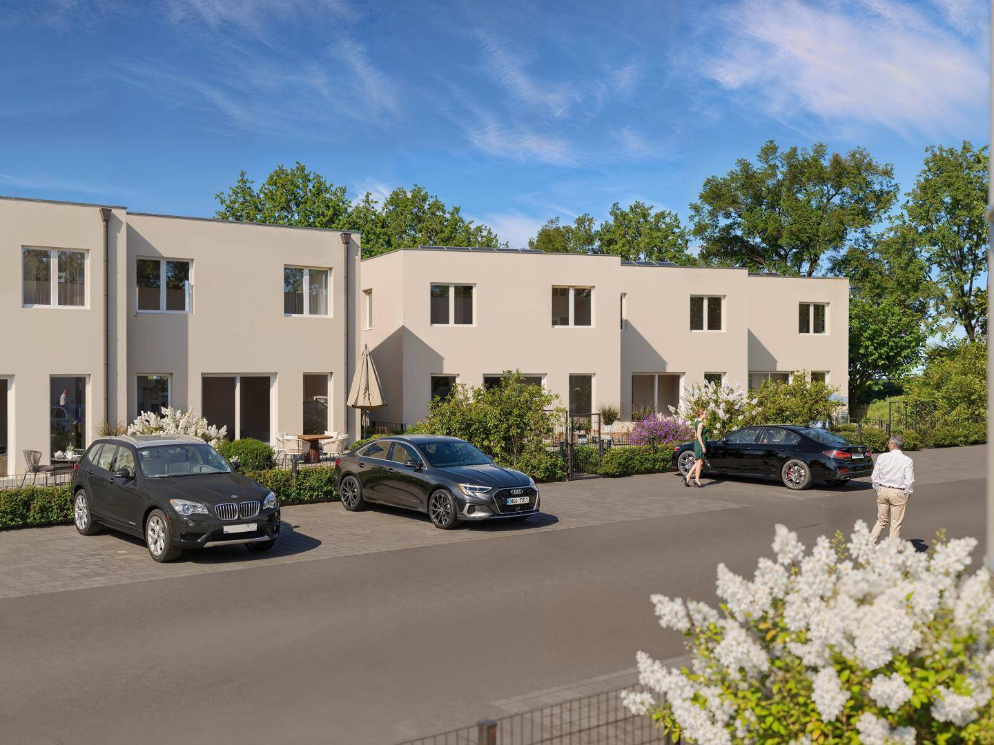 Reihenhäuser mit hellen Fassaden und gepflasterten Parkplätzen in einer grünen Umgebung.