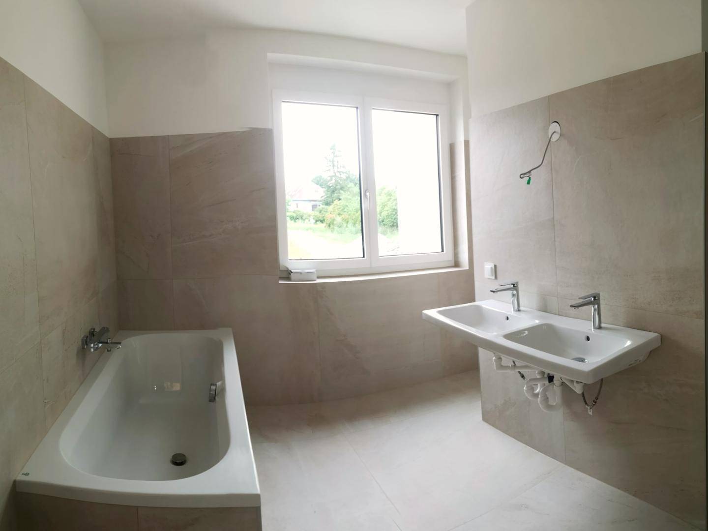Modernes Badezimmer mit Badewanne, Doppelwaschbecken und Fenster für Tageslicht.