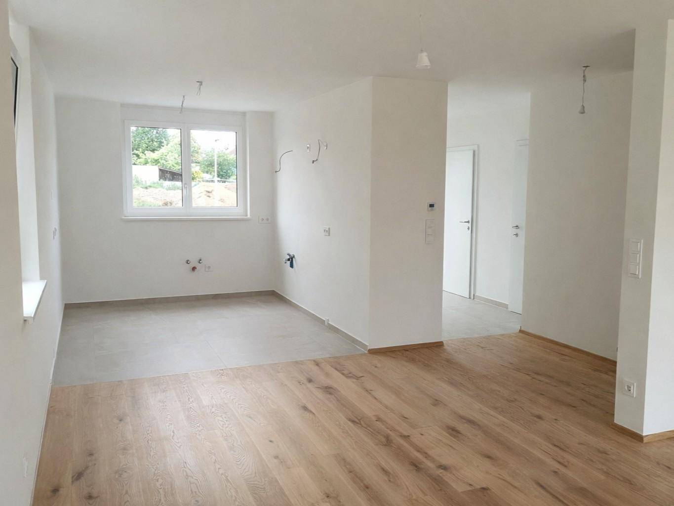 Heller, unmöblierter Wohnbereich mit neuem Holzboden und Fensterblick ins Grüne.