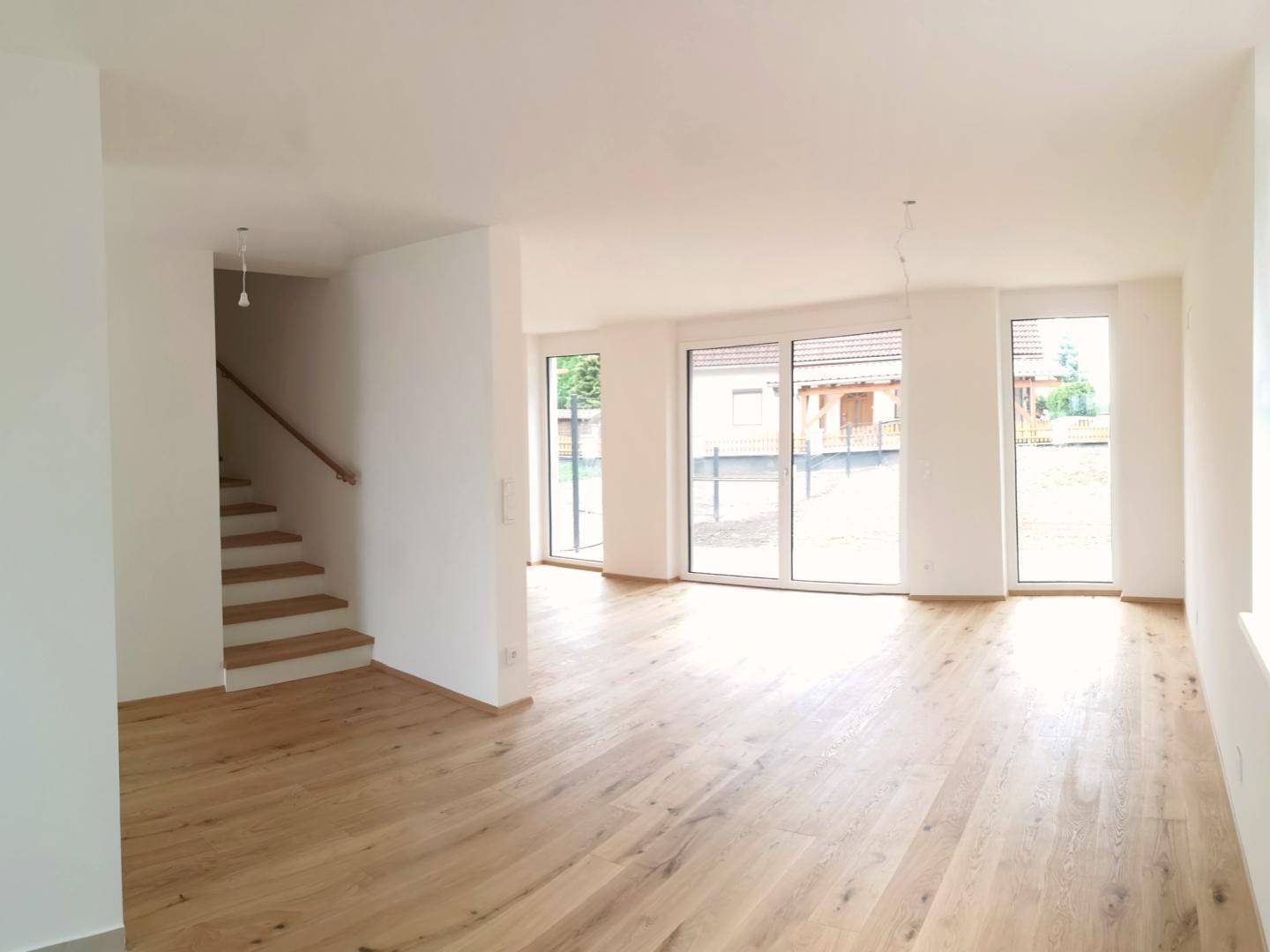 Geräumiger Wohnbereich mit Eichenparkett, großen Fensterfronten und Treppenaufgang.