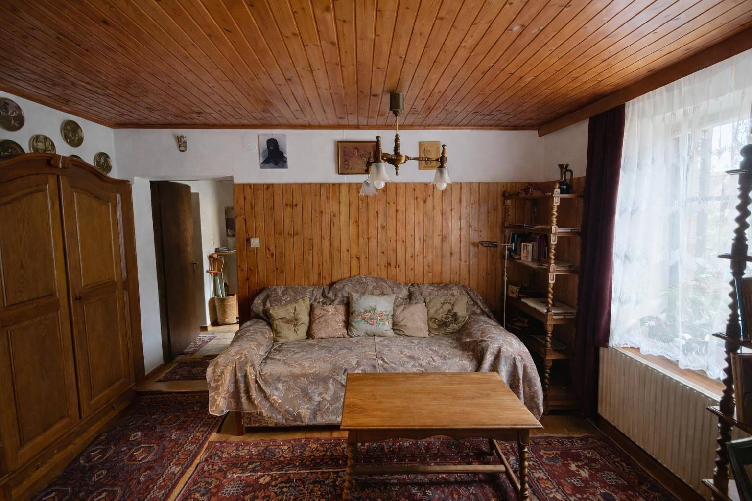 Wohnzimmer mit Holzvertäfelung, Holzdecke und traditionellen Möbeln, durchflutet von Tageslicht.
