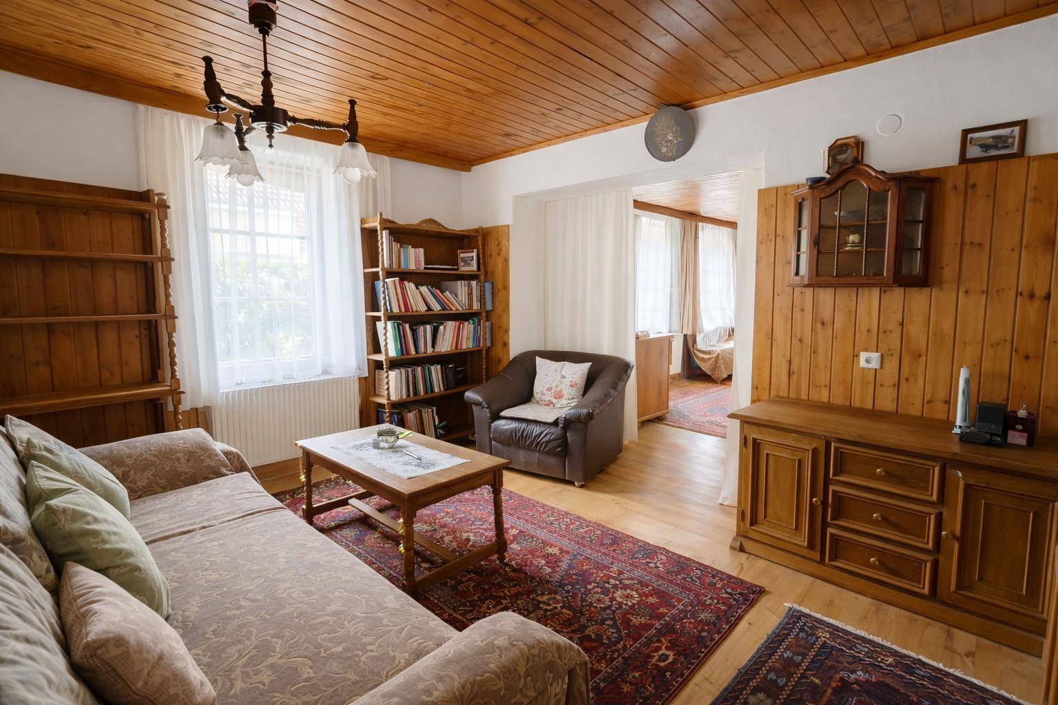 Gemütliches Wohnzimmer im Landhausstil mit Holzdecke, Teppichen und Bücherregalen.